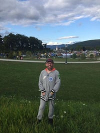 Gerry, a man with a disability and light skin tone, stands in a grassy field while smiling.