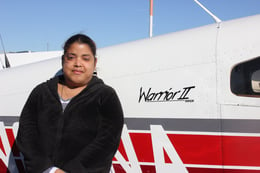 Jerrilis, a woman with a disability and a medium skin tone, stands in front of a lightweight plane named the Warrior Two.