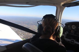 Jerrilis, a woman with a disability and a medium skin tone, looks out to the Pioneer Valley from the cockpit of a lightweight plane.