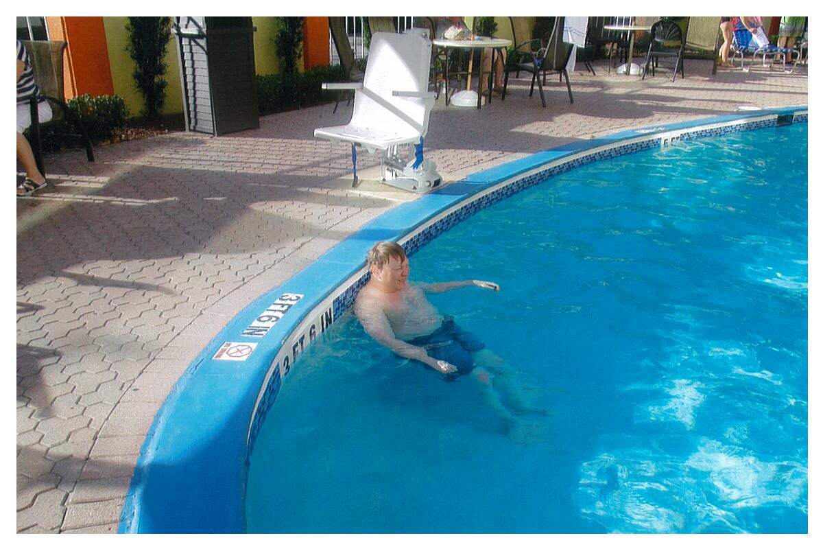 Michael, a man with a disability and a light skin tone, relaxes at the edge of a hotel pool in Florida.