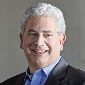 Portrait of Interim Executive Director Keith Kendall, an older man with a light skin tone and short, wavy, white hair, is smiling while looking off to the side.