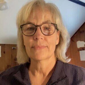 Portrait of Director of Development & Communications, an older woman with light skin tone and shoulder length, grey hair, and glasses.